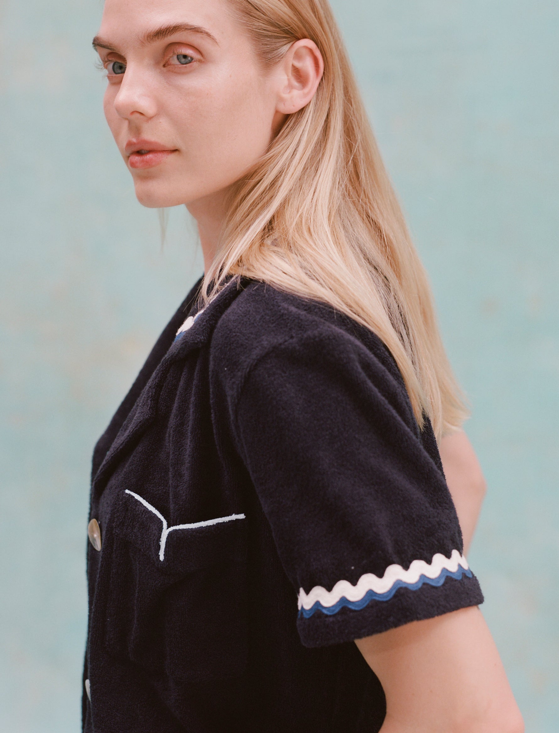 Female model with long blonde hair turned to the side with her face towards the camera wearing the 'Rick Rack' Cabana ~ Crop Cut (Midnight Blue), shot on a textured light blue background.