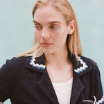 Female model with long blonde hair wearing the 'Rick Rack' Cabana ~ Crop Cut (Midnight Blue) unbuttoned with a white shirt, shot on a textured light blue background.