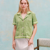 Female model with long blonde hair wearing the 'Rick Rack' Cabana ~ Crop Cut (Green) buttoned with a white full-length silk dress, all shot on a textured light blue background.