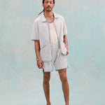 Male model with dreadlocks wearing the 'Standard Issue' Cabana (Sky Blue) fully unzipped with a white tank top underneath that is tucked into matching 'standard issue' shorts in Sky Blue with white slippers, all shot on a light blue background.