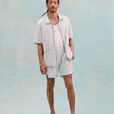 Male model with dreadlocks wearing the 'Standard Issue' Cabana (Sky Blue) fully unzipped with a white tank top underneath that is tucked into matching 'standard issue' shorts in Sky Blue with white slippers, all shot on a light blue background.