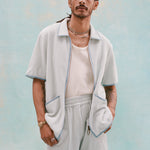Male model with dreadlocks wearing a 'Standard Issue' Cabana (Sky Blue) that is fully unzipped, a white tank top underneath it tucked into matching 'Standard Issue' Sky blue shorts, all shot on a light blue background.