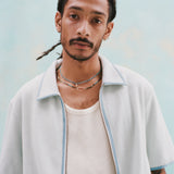 Male mode with dreadlocks wearing the 'Standard Issue' Cabana (Sky Blue) fully unzipped with a white tank top underneath, shot against a light blue background.