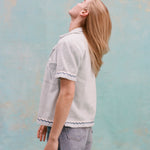 Female model with long blonde hair turned away from the camera, wearing the 'Rick Rack' Cabana ~ Crop Cut (Sky Blue) with jean shorts, shot on a light blue textured background.