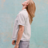 Female model with long blonde hair turned away from the camera, wearing the 'Rick Rack' Cabana ~ Crop Cut (Sky Blue) with jean shorts, shot on a light blue textured background.