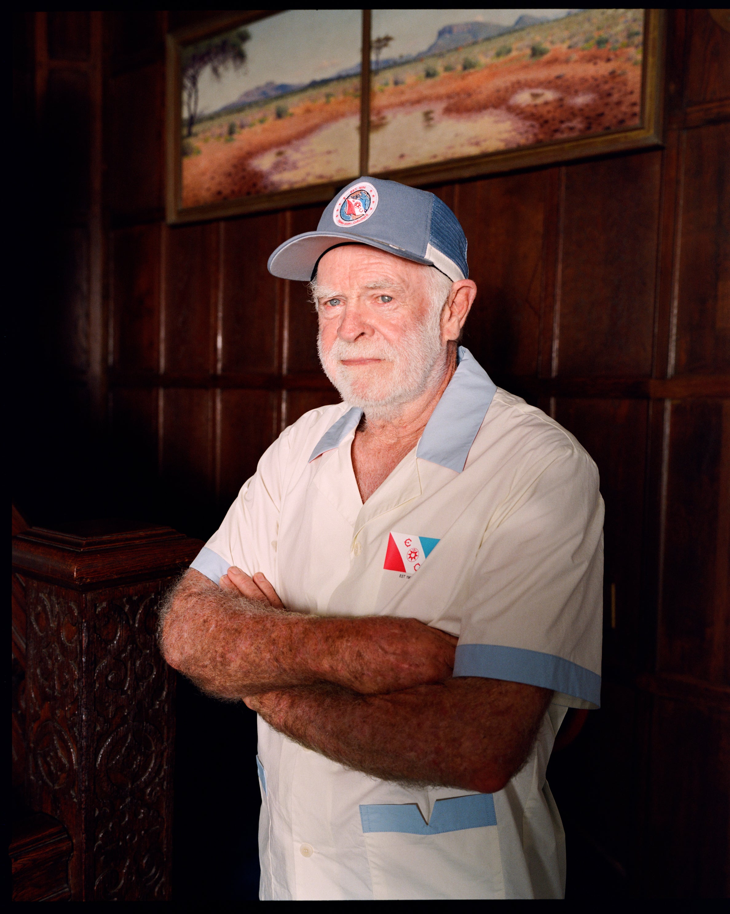 Older gentleman wearing the 'Explorer's Club' Field Uniform and our 'Explorers Club' 5-Panel Souvenir Cap. His arms are crossed. 