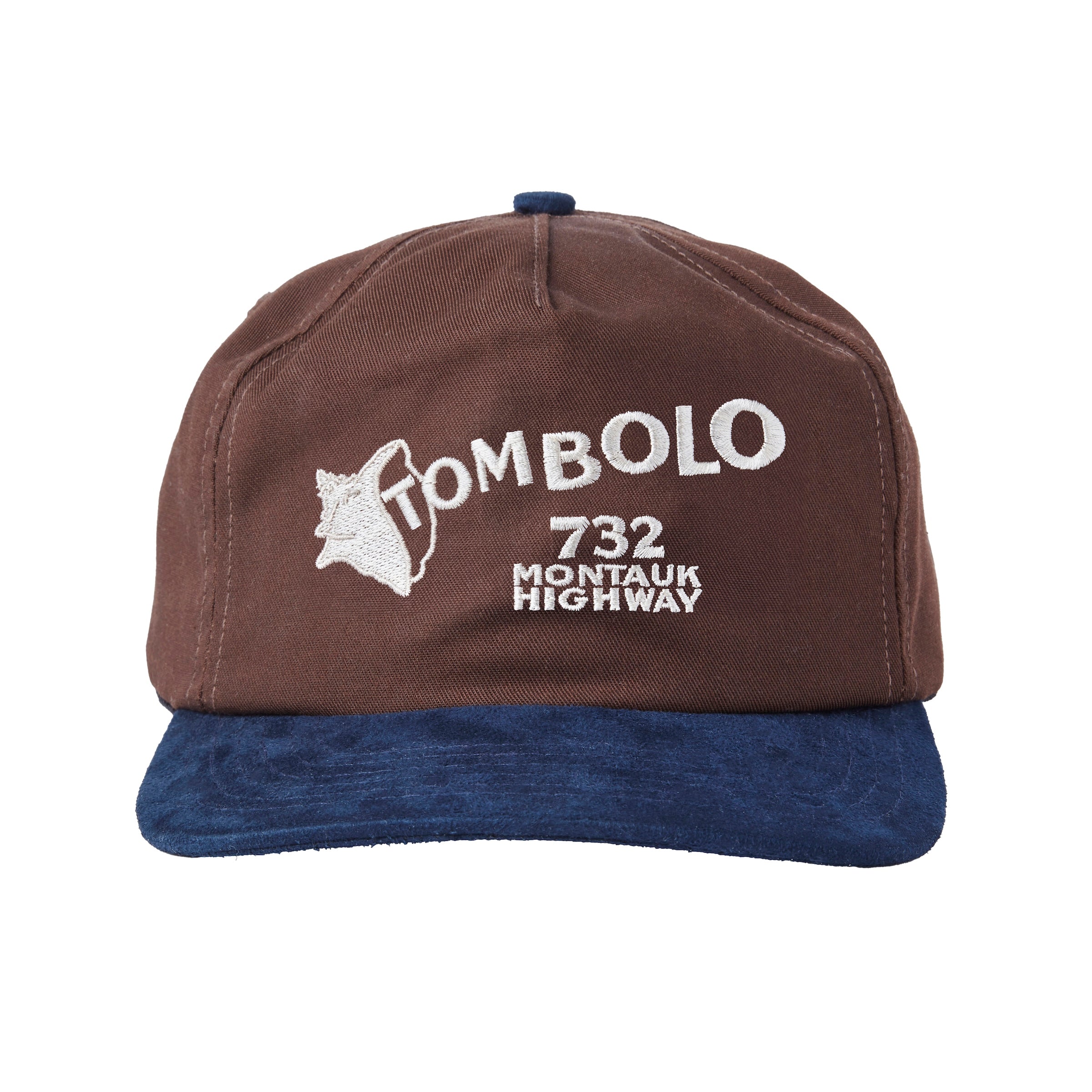 A brown baseball cap with a navy blue brim. The front features white embroidered text that reads “TOMBOLO” with a seashell illustration forming the letter “T,” and below it, “732 MONTAUK HIGHWAY.”