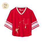 Red mesh crop-cut shirt with white stripes on the sleeves, a white V-neck, and an embroidered football design showing a player kicking a football toward a goalpost outlined around the chest pocket.