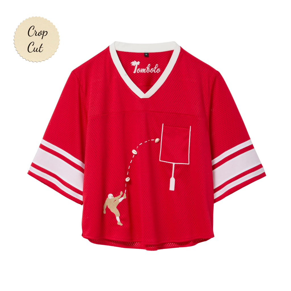Red mesh crop-cut shirt with white stripes on the sleeves, a white V-neck, and an embroidered football design showing a player kicking a football toward a goalpost outlined around the chest pocket.