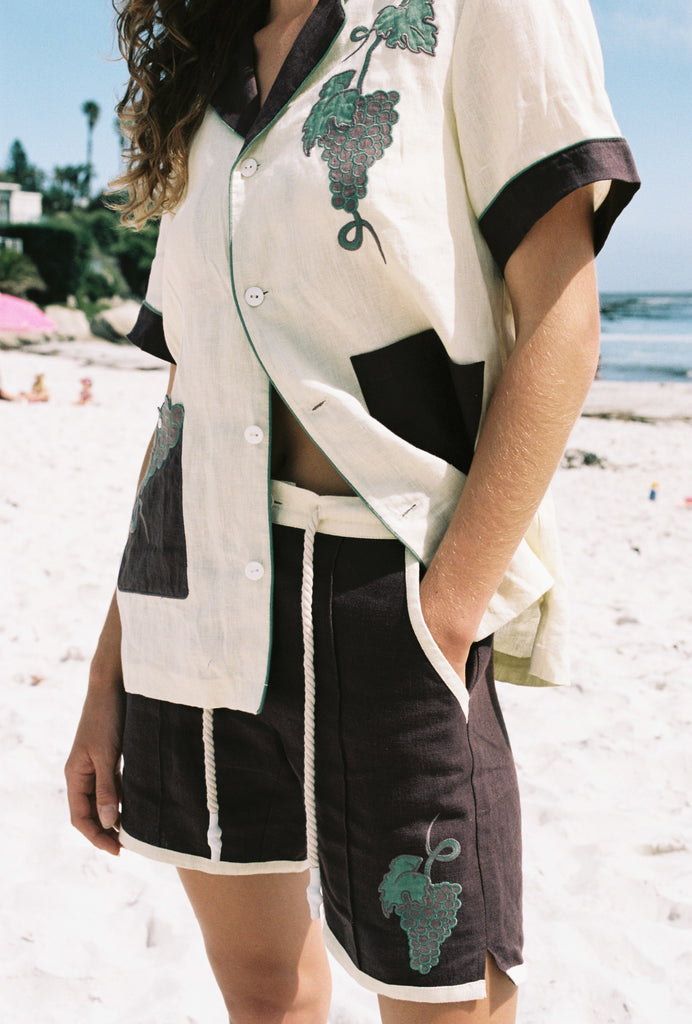 Female model wearing full 'Tombarolo' cabana set on the beach. Shirt half unbuttoned.
