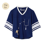 Navy blue mesh crop-cut shirt with white stripes on the sleeves, a white V-neck, and an embroidered football design showing a player kicking a football toward a goalpost outlined around the chest pocket.