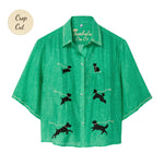 Green cropped cabana shirt with black dog silhouettes across the front, each attached to a white leash motif, with white piping along the collar and sleeves.