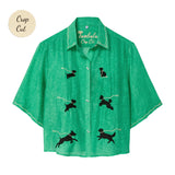 Green cropped cabana shirt with black dog silhouettes across the front, each attached to a white leash motif, with white piping along the collar and sleeves.