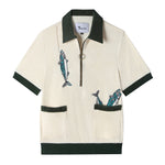 Front view of our Angler Cabana Shirt in cream with forest green on the collar, pockets, and bottom waistband, embroidered with a fish and a hook on the top left and two fish coming out of the bottom right pocket as well as featuring an antique brass half zip