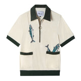 Front view of our Angler Cabana Shirt in cream with forest green on the collar, pockets, and bottom waistband, embroidered with a fish and a hook on the top left and two fish coming out of the bottom right pocket as well as featuring an antique brass half zip
