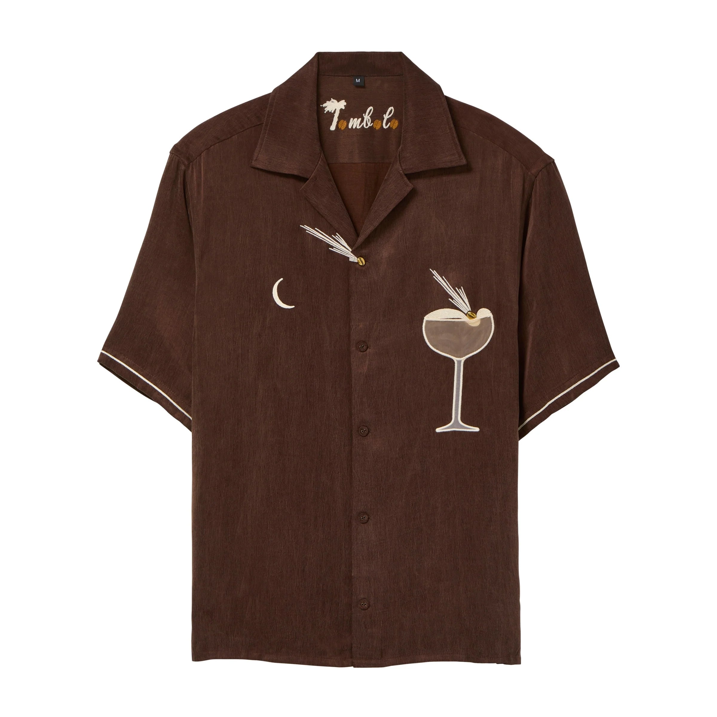Brown short-sleeve cabana shirt with embroidered cocktail motifs, including a crescent moon and a coupe glass with garnish. The shirt has cream piping on the sleeves and “Tombolo” embroidery at the collar.