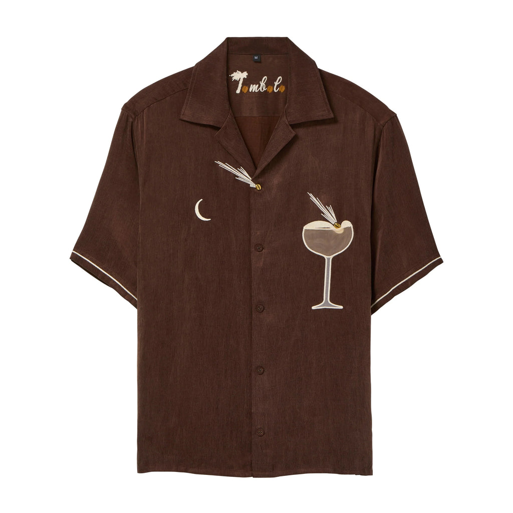 Brown short-sleeve cabana shirt with embroidered cocktail motifs, including a crescent moon and a coupe glass with garnish. The shirt has cream piping on the sleeves and “Tombolo” embroidery at the collar.