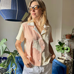 Aemilia wearing the conched out shirt and sunglasses looking out of an apartment window with a ray of light shining across her