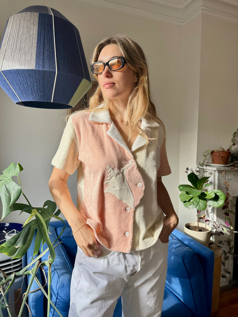 Aemilia wearing the conched out shirt and sunglasses looking out of an apartment window with a ray of light shining across her