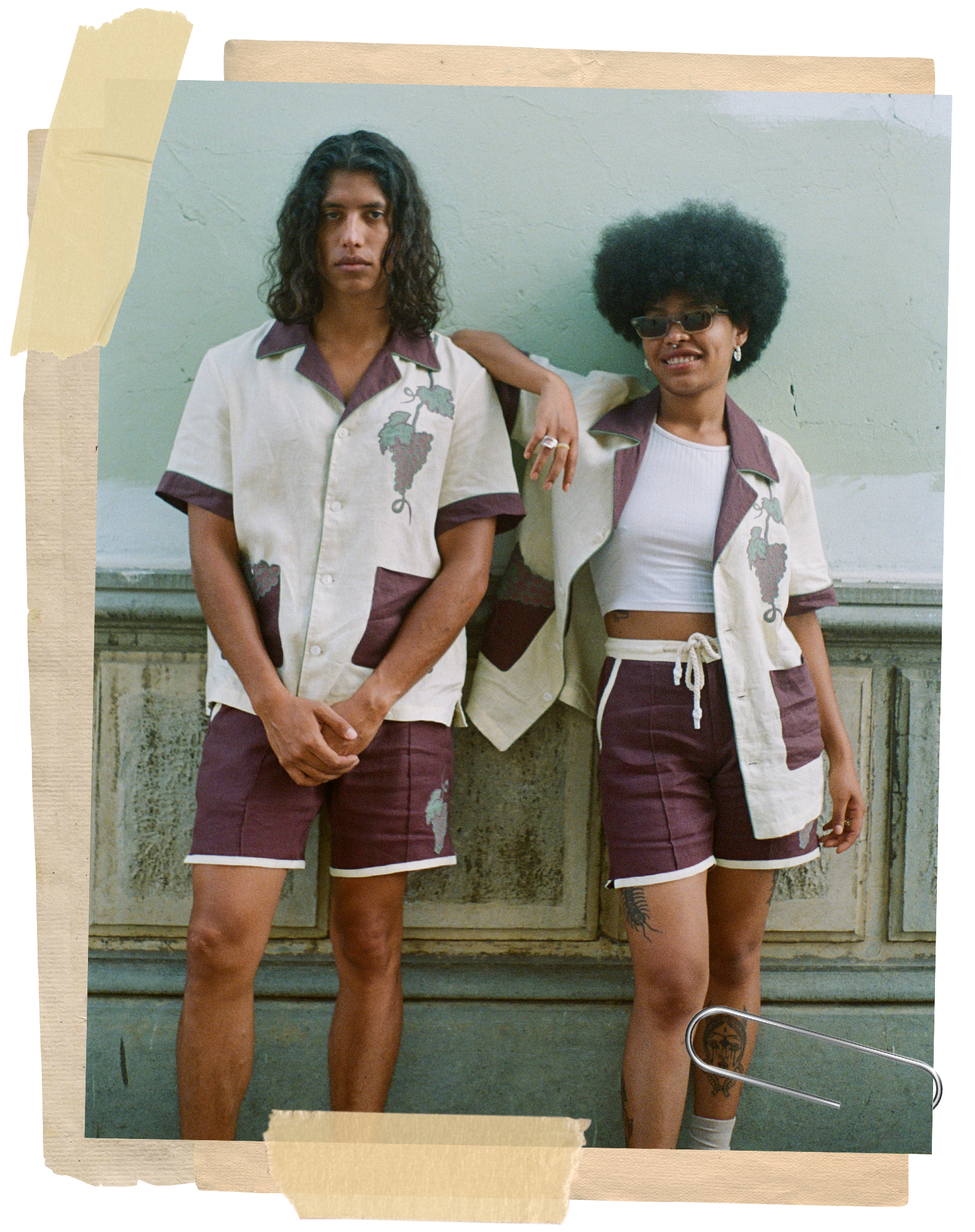 Woman smiles as she leans on man, both wearing the full wine-themed linen Tombolo set. Man wears his shirt fully buttoned and woman wears it casually unbuttoned with a white tank top underneath. 