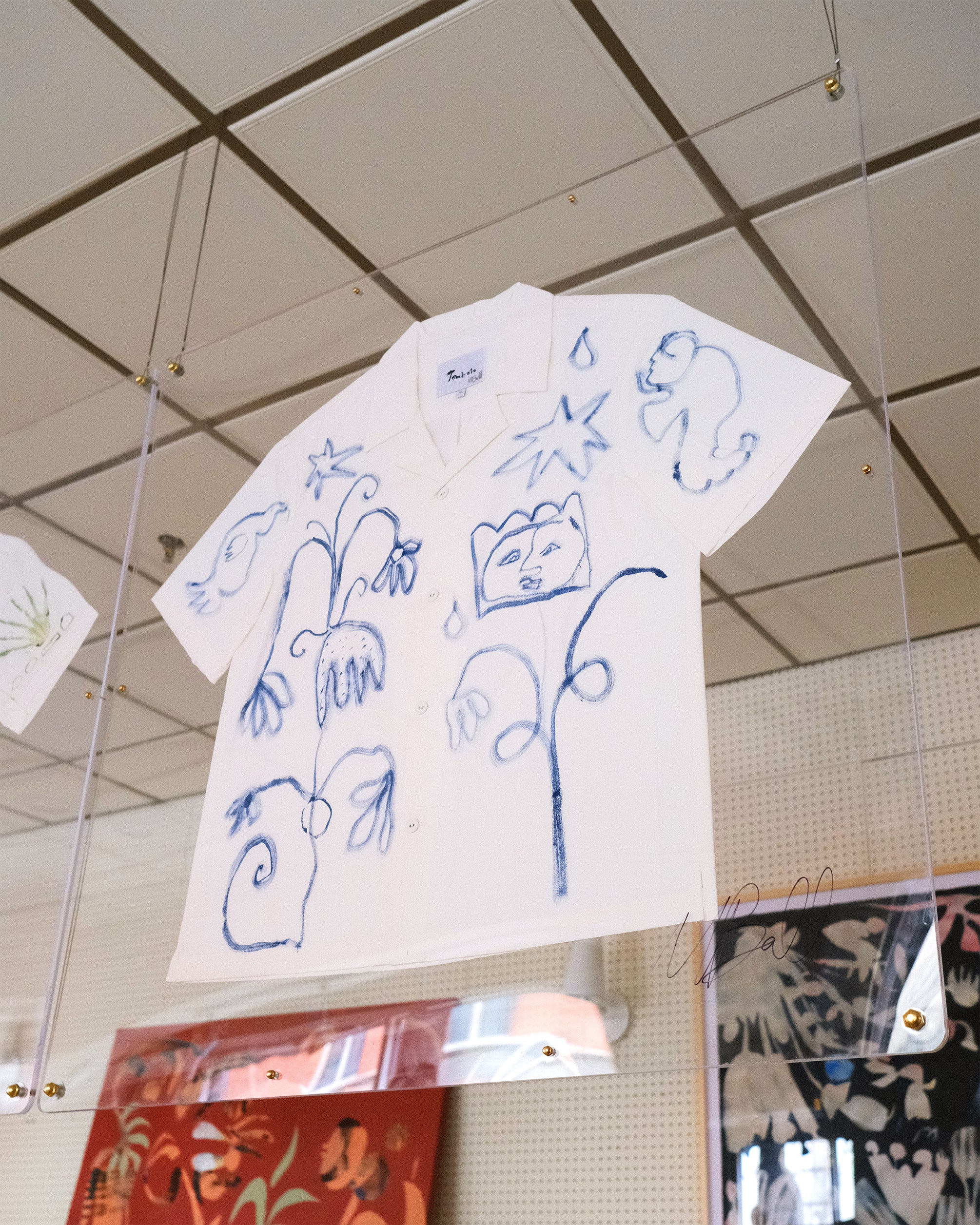 A short-sleeve white shirt with blue botanical and abstract designs, displayed inside a glass case.