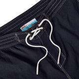 Close-up of navy board shorts with lace-up waist and interior label reading 'Whaler by Tombolo' with a boat and ocean graphic.