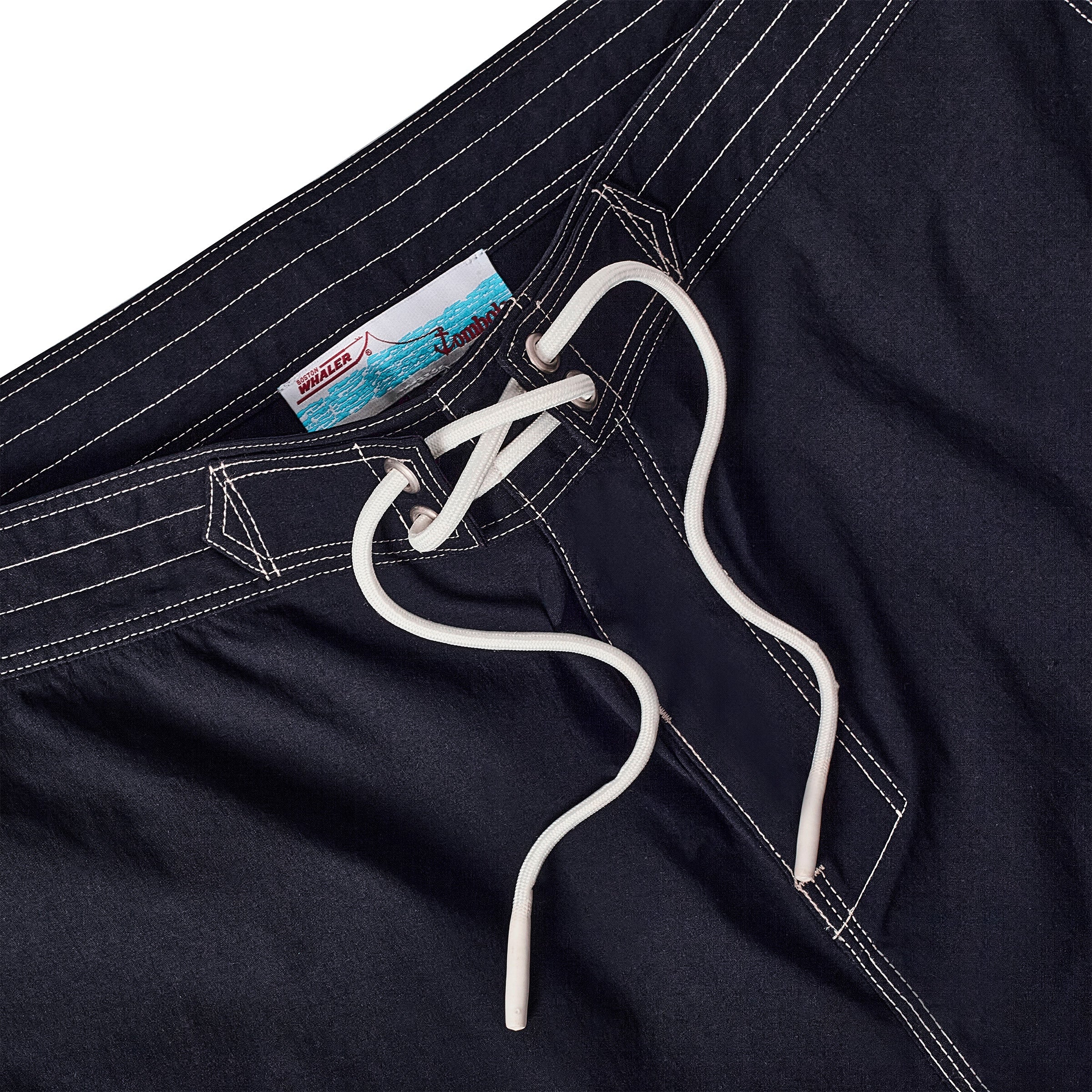 Close-up of navy board shorts with lace-up waist and interior label reading 'Whaler by Tombolo' with a boat and ocean graphic.