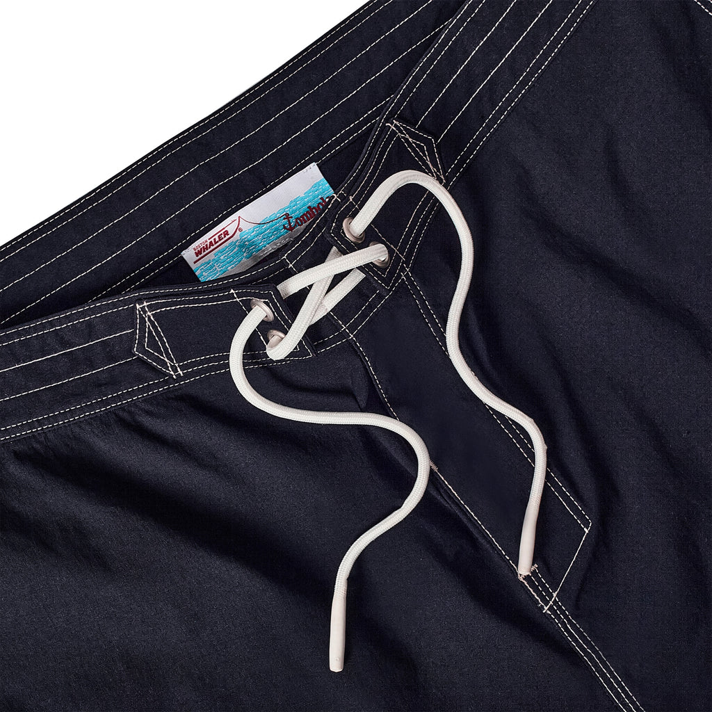 Close-up of navy board shorts with lace-up waist and interior label reading 'Whaler by Tombolo' with a boat and ocean graphic.