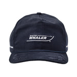 Front view of a navy blue baseball cap with white embroidered text and logo reading “Boston Whaler,” styled to resemble the outline of a boat. The brim features subtle distressed detailing, and there is a thin blue rope accent above the brim. White embroidered stripes appear on the sides of the cap.