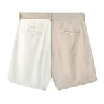 Back view of two-tone pleated shorts in beige and off-white. Features include belt loops, two welt pockets with button closures, and a small rectangular 'Tombolo' logo patch above the left pocket.