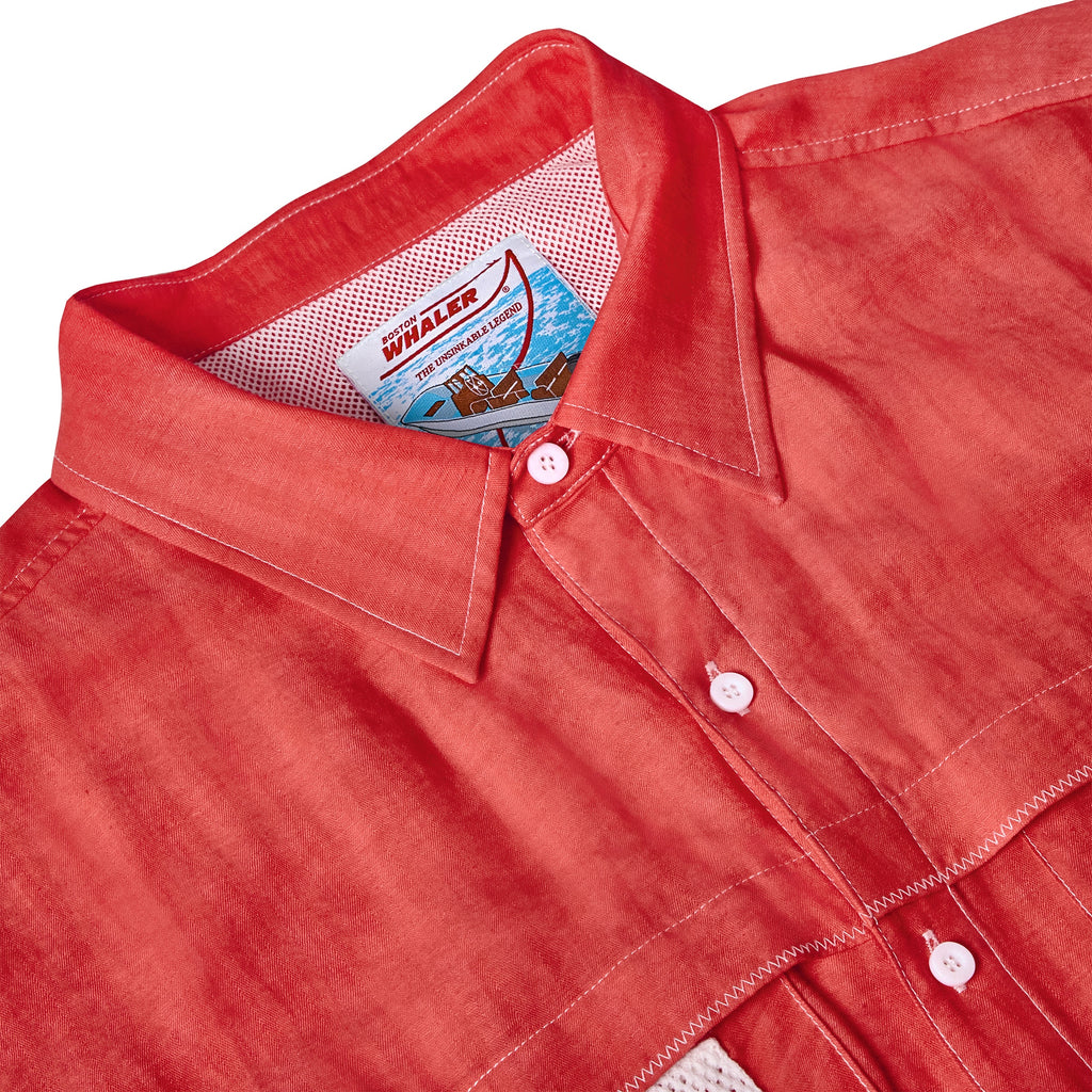 Close-up of the collar on a red button-down shirt featuring white contrast stitching and buttons. Inside the collar is a mesh lining and a woven label that reads 'Boston Whaler' above an illustrated boating scene.