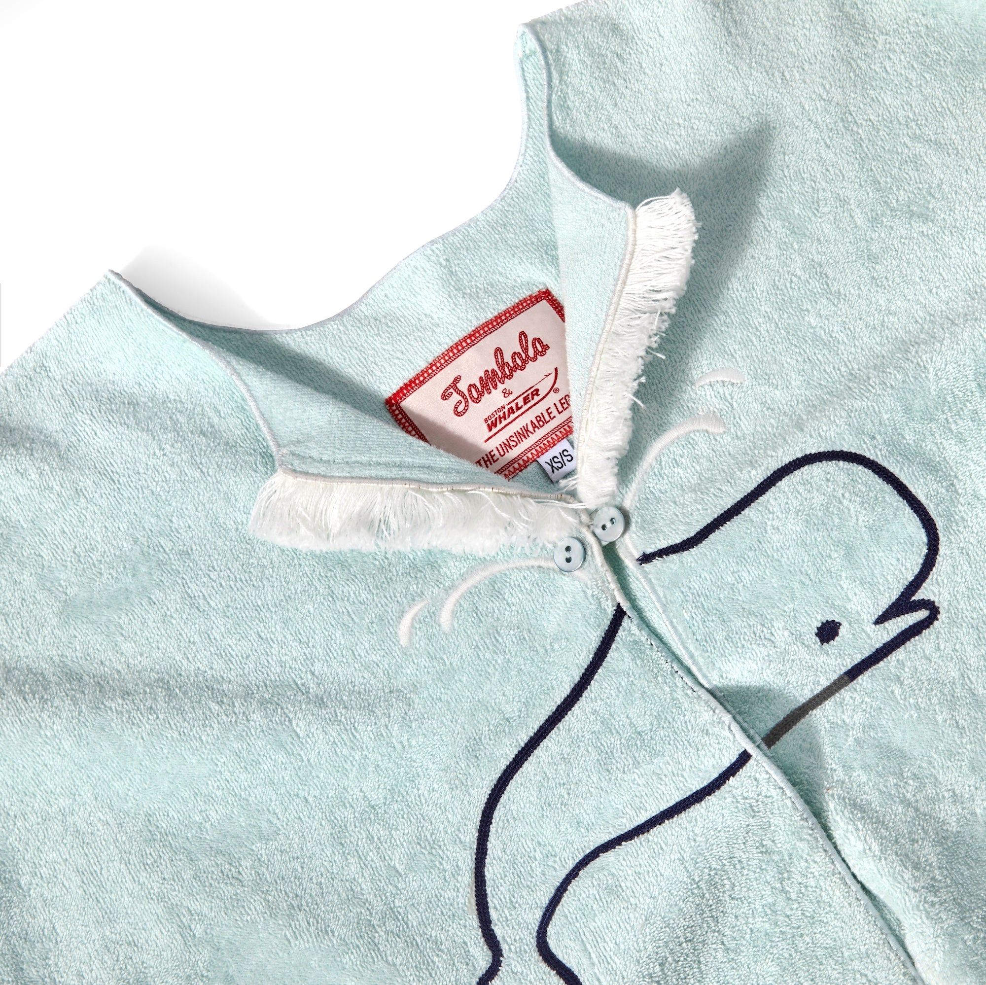 Close-up product image of the 'Boston Whaler' Hand Towel Top's interior label tag, and its chain stitched sperm whale. 