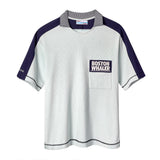 Light blue cotton mesh short-sleeve shirt with navy shoulder panels and a striped ribbed collar. Features a navy chest pocket with white 'Boston Whaler' embroidery and navy contrast stitching on the cuffs and hem. 