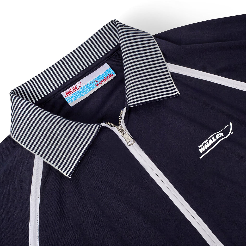Close-up of a navy sun shirt with a white quarter zip, white piping, and a navy-and-white striped collar. The chest features the Boston Whaler logo, and the neck tag includes branding for both 'Boston Whaler' and 'Tombolo'.