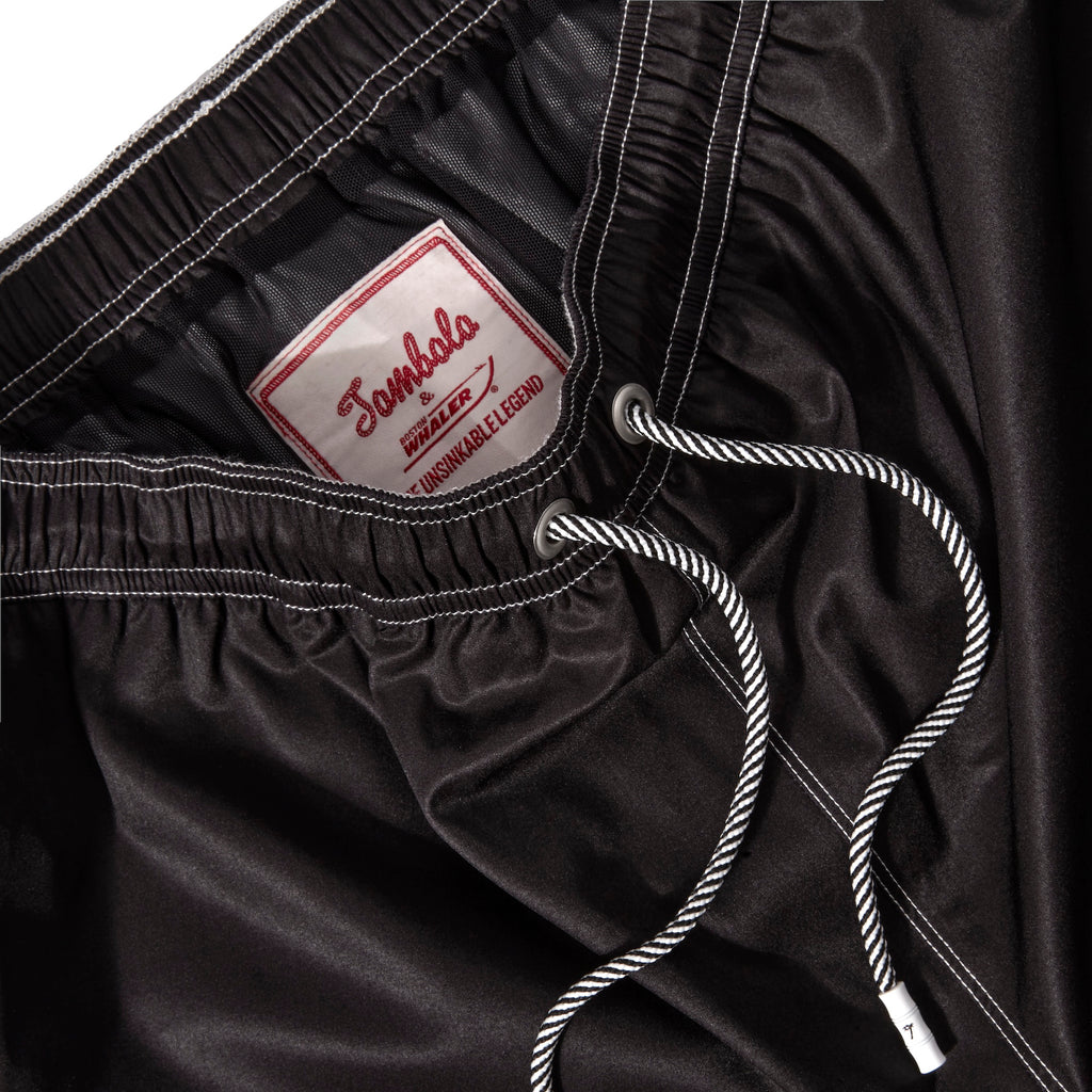 Close up product image of the 'boston whaler' swim trunks' interior label and metal eyelet stoppers on white and black twist drawstrings.