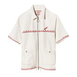 A white short-sleeved 'Boston Whaler' branded shirt with red chainstitched harpoon hull stripe on cuffs and bottom sweep, featuring a two-way nickel zipper with ring pull and front patch pockets with nickel snaps.