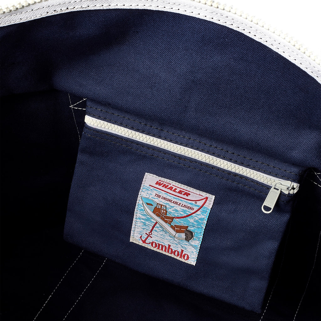 Close-up of interior pocket of navy canvas tote. 'Boston Whaler' and 'Tombolo' co-branded label is visible on the pocket.