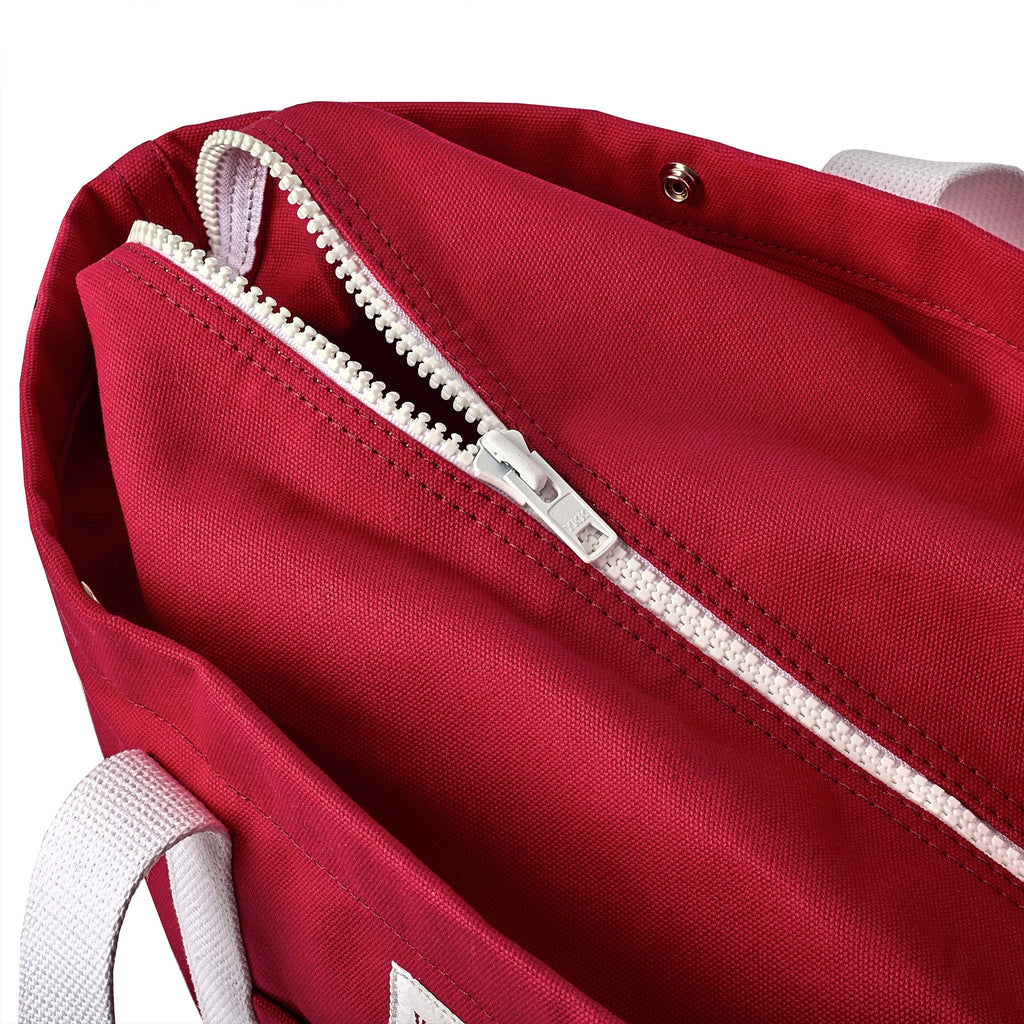 Close-up of red canvas tote's white zipper. 