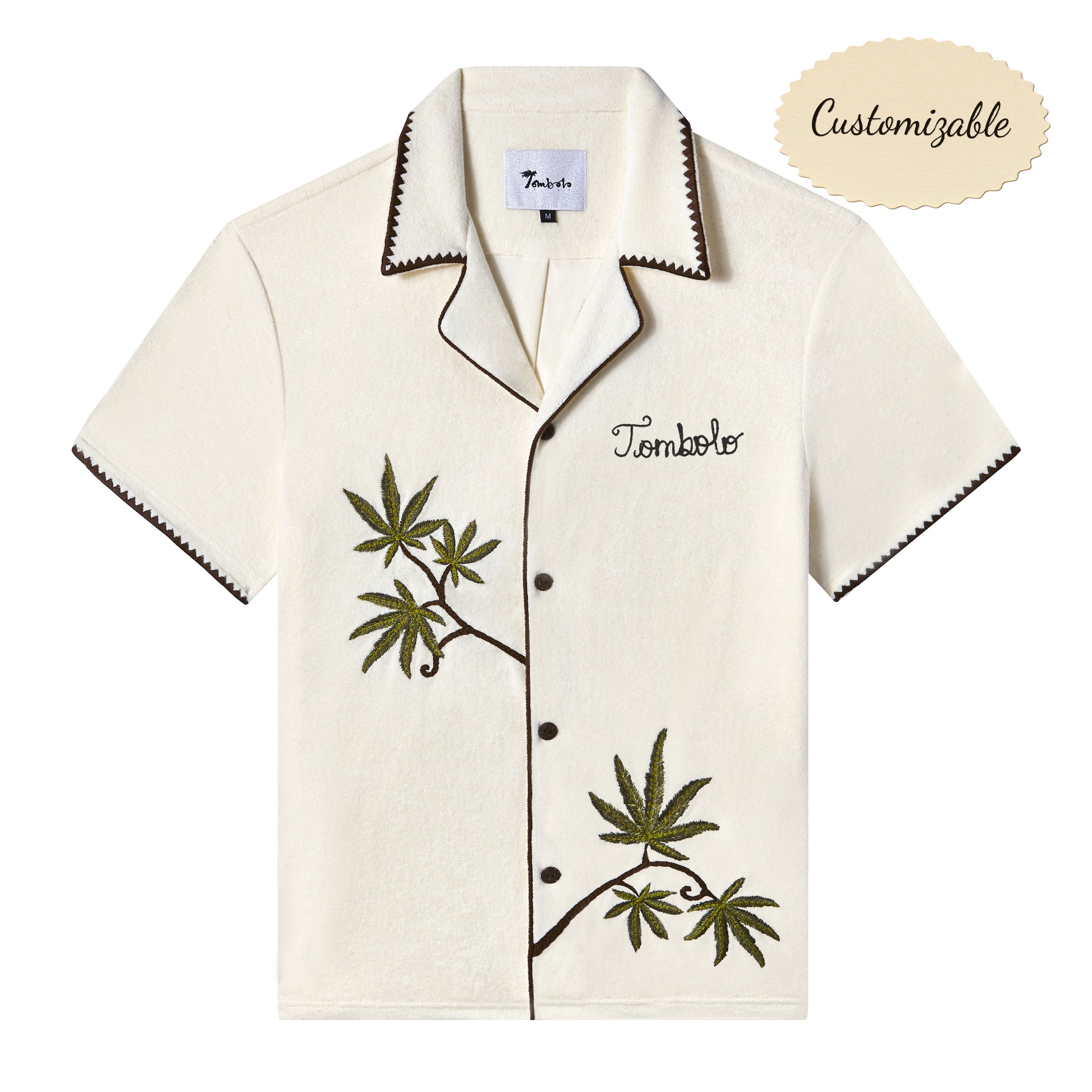 Short-sleeve cream cabana shirt with brown trim, embroidered green leaves, and the word 'Tombolo' stitched on the chest. Shirt is labeled customizable.