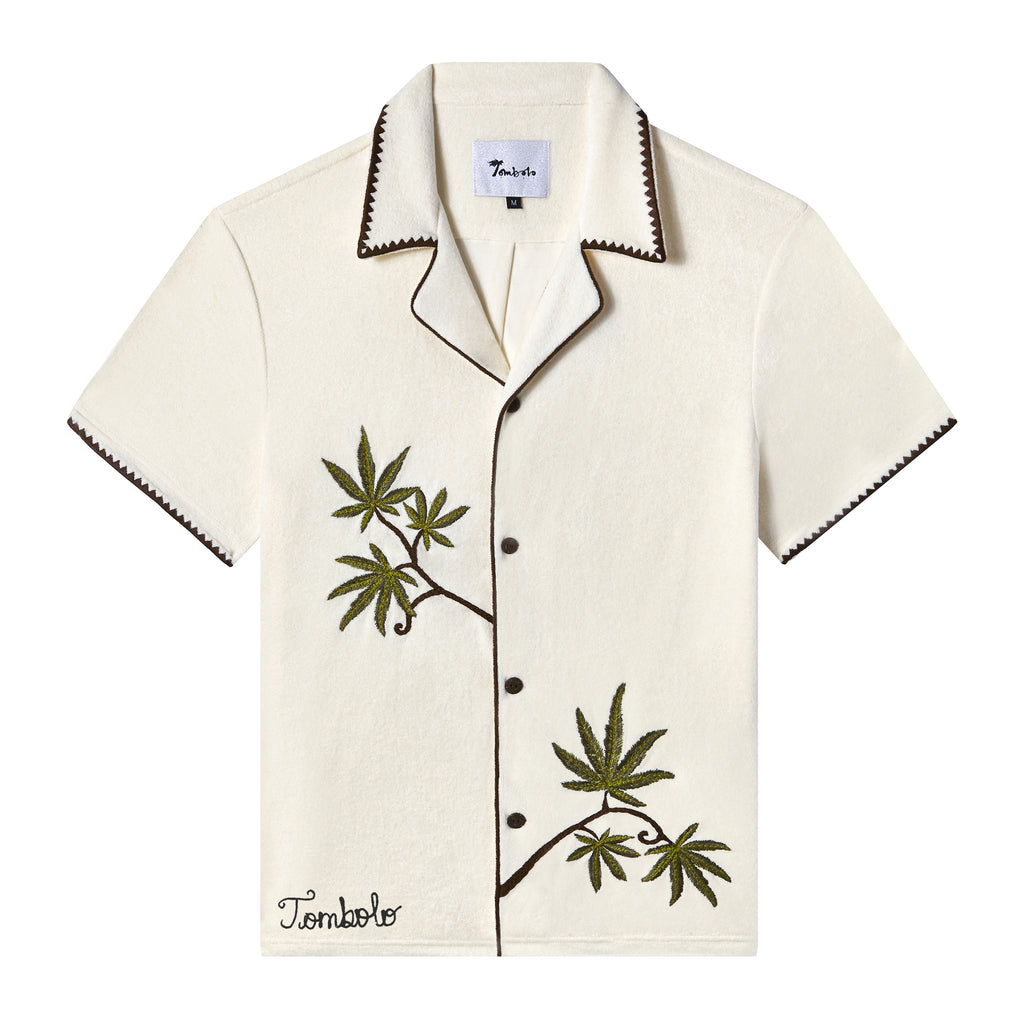 Short-sleeve cream cabana shirt with brown trim, embroidered green leaves, and the word 'Tombolo' on the wearer's lower right.