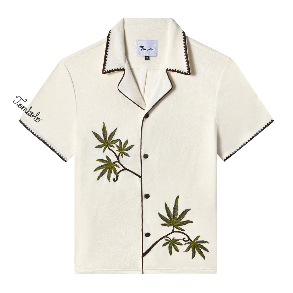 Short-sleeve cream cabana shirt with brown trim, embroidered green leaves, and the word 'Tombolo' stitched on the wearer's right sleeve.