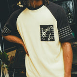 Man wearing black and cream SNL terry t-shirt in front of a bar cabinet.