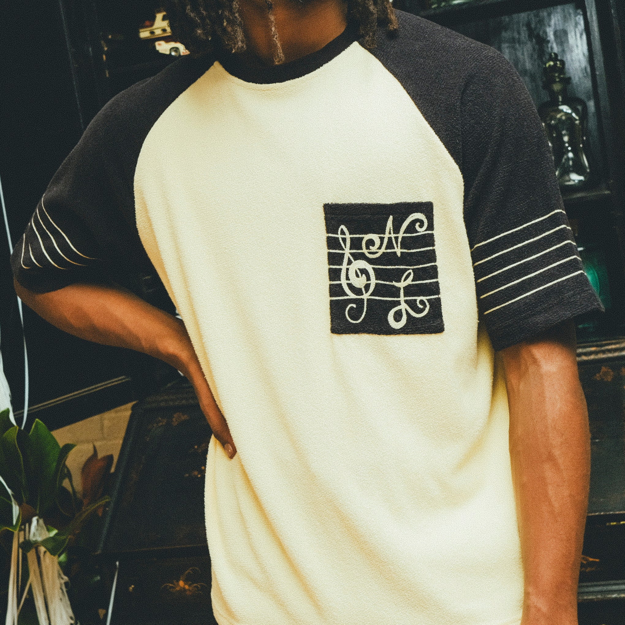 Man wearing black and cream SNL terry t-shirt in front of a bar cabinet.