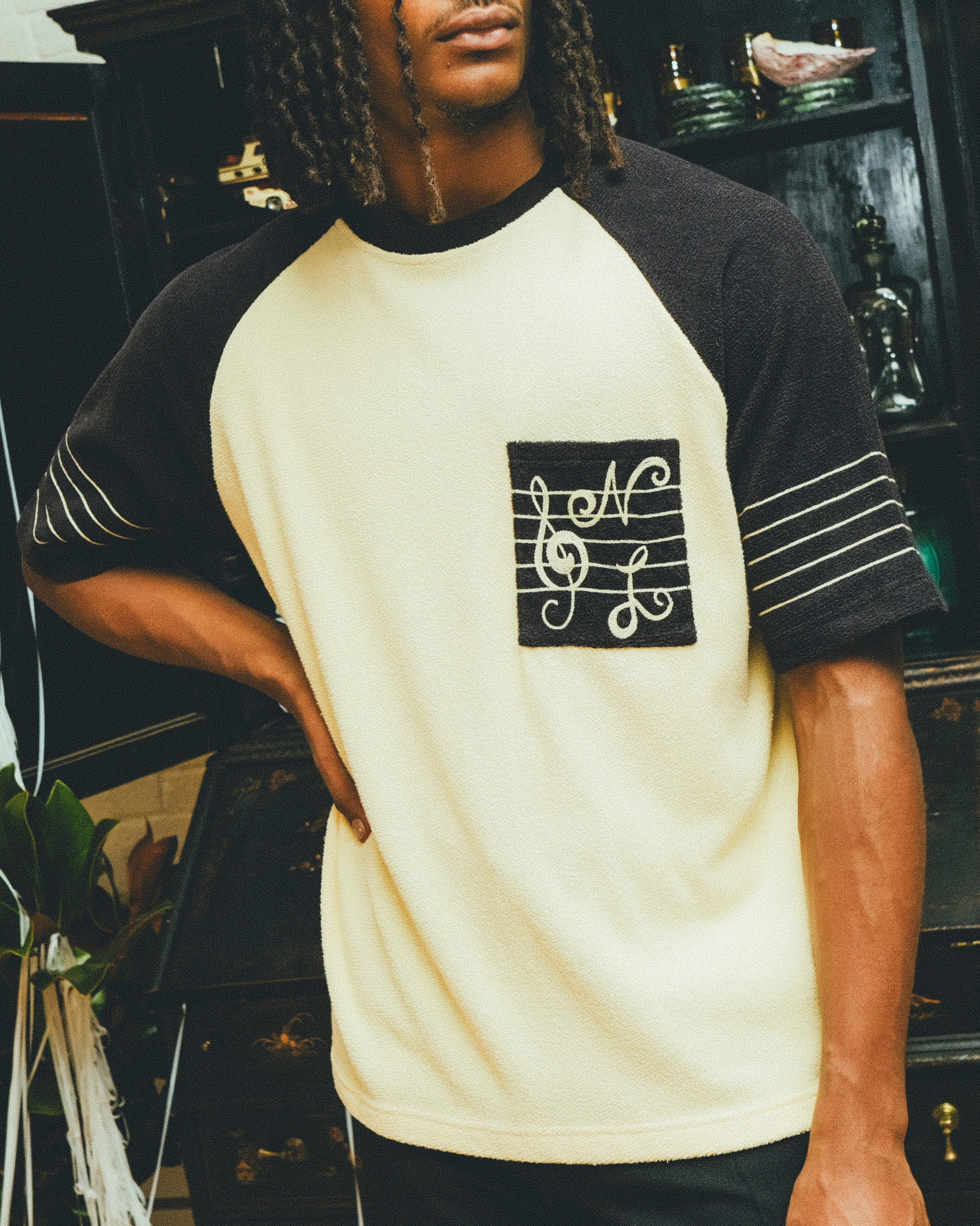 Man wearing black and cream SNL terry t-shirt in front of a bar cabinet.