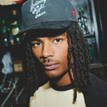 Model wearing a black cap with 'Saturday Night Live' embroidery.