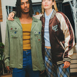 Two models standing together, wearing the SNL Long Sleeve 1976 shirt and the Souvenir Jacket. 