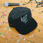 Black cap with 'Saturday Night Live' embroidery on a wooden floor with confetti and a microphone.