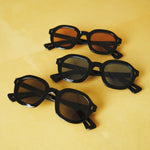 Three variations of the Lesca Lunetier X Tombolo lenses, all of which have a black frame and different lens colors (charcoal, azure, and coral) with front-facing product images in charcoal with emphasis on the different colors of lenses on a yellow background. 