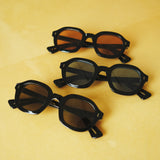 Three variations of the Lesca Lunetier X Tombolo lenses, all of which have a black frame and different lens colors (charcoal, azure, and coral) with front-facing product images in charcoal with emphasis on the different colors of lenses on a yellow background. 