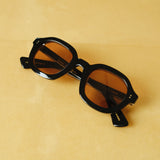 Lesca Lunetier X Tombolo front-facing product image with a black frame and squared round lenses in coral coloring on a yellow background.